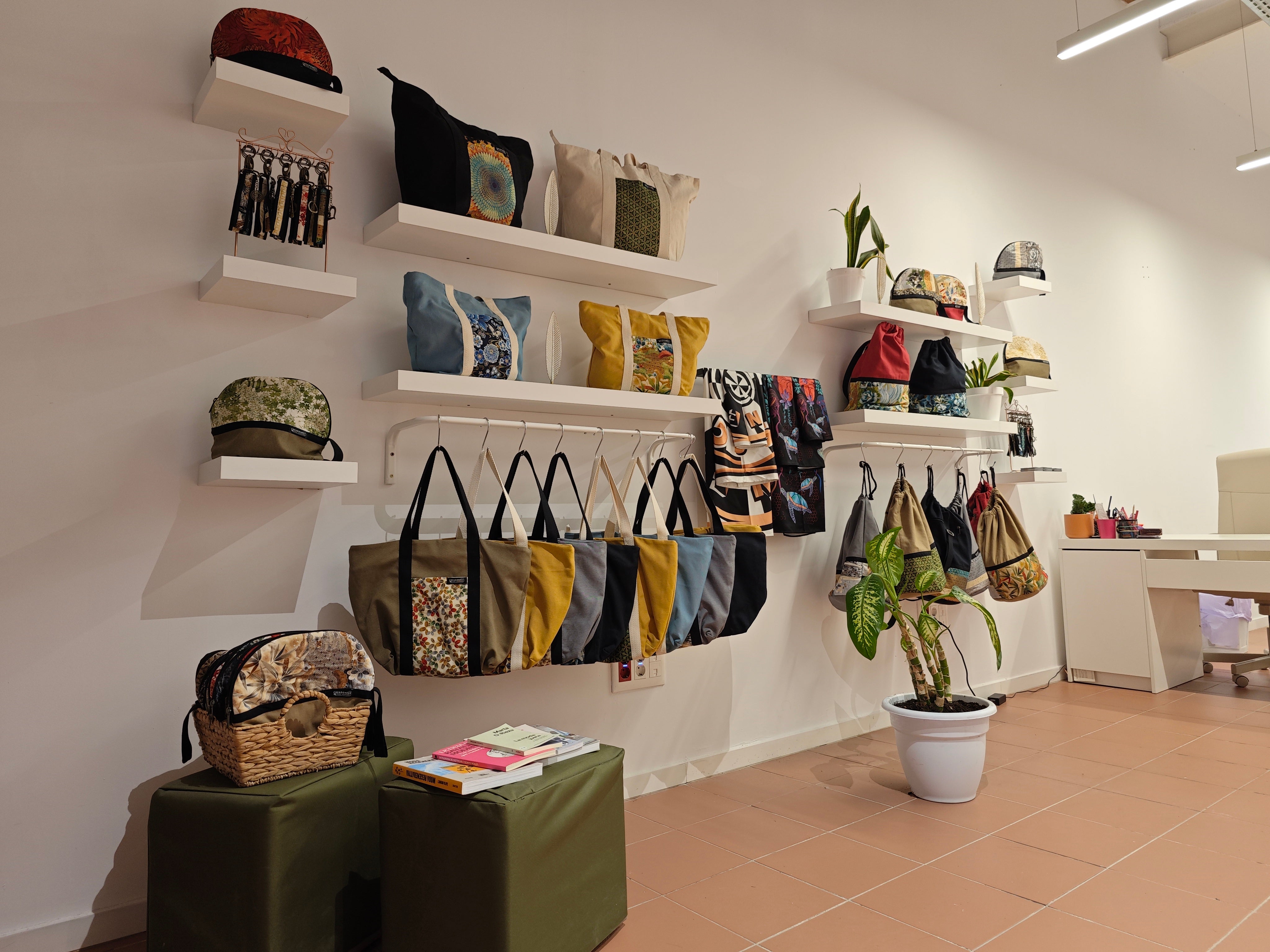 Tienda de Creadoness con bolsos y accesorios exhibidos en estanterías blancas, en un espacio moderno y minimalista con decoración natural.
