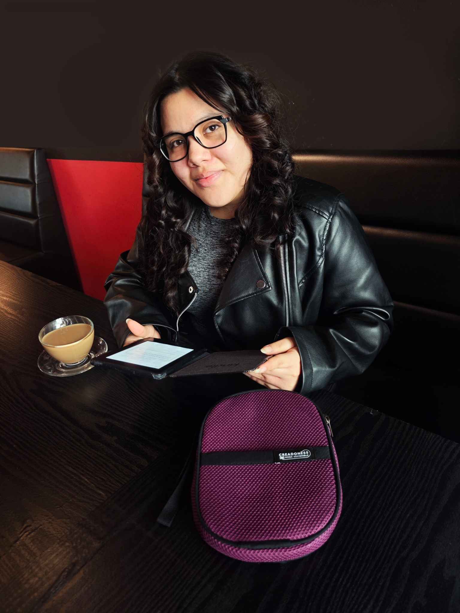 chica en cafeteria leyendo su e-book, con su funda en el lado izquierdo y un cafe en el lado derecho de la mesa