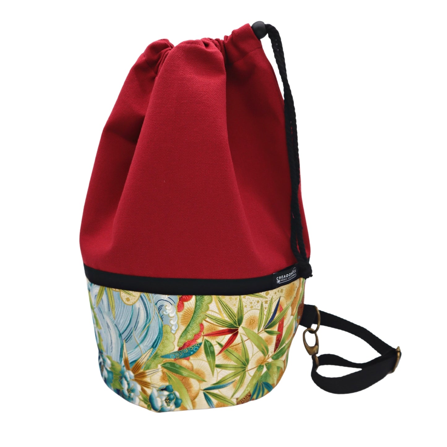 Mochila Petate de base circular de 24 cm de diámetro hecha de algodón. Su medida es de 38 cm de alto y 37 cm de ancho. Posee un asa bandolera para cruzar. En el interior tiene un bolsillo de 26 cm y un bolsillo oculto de 15 cm de profundidad.