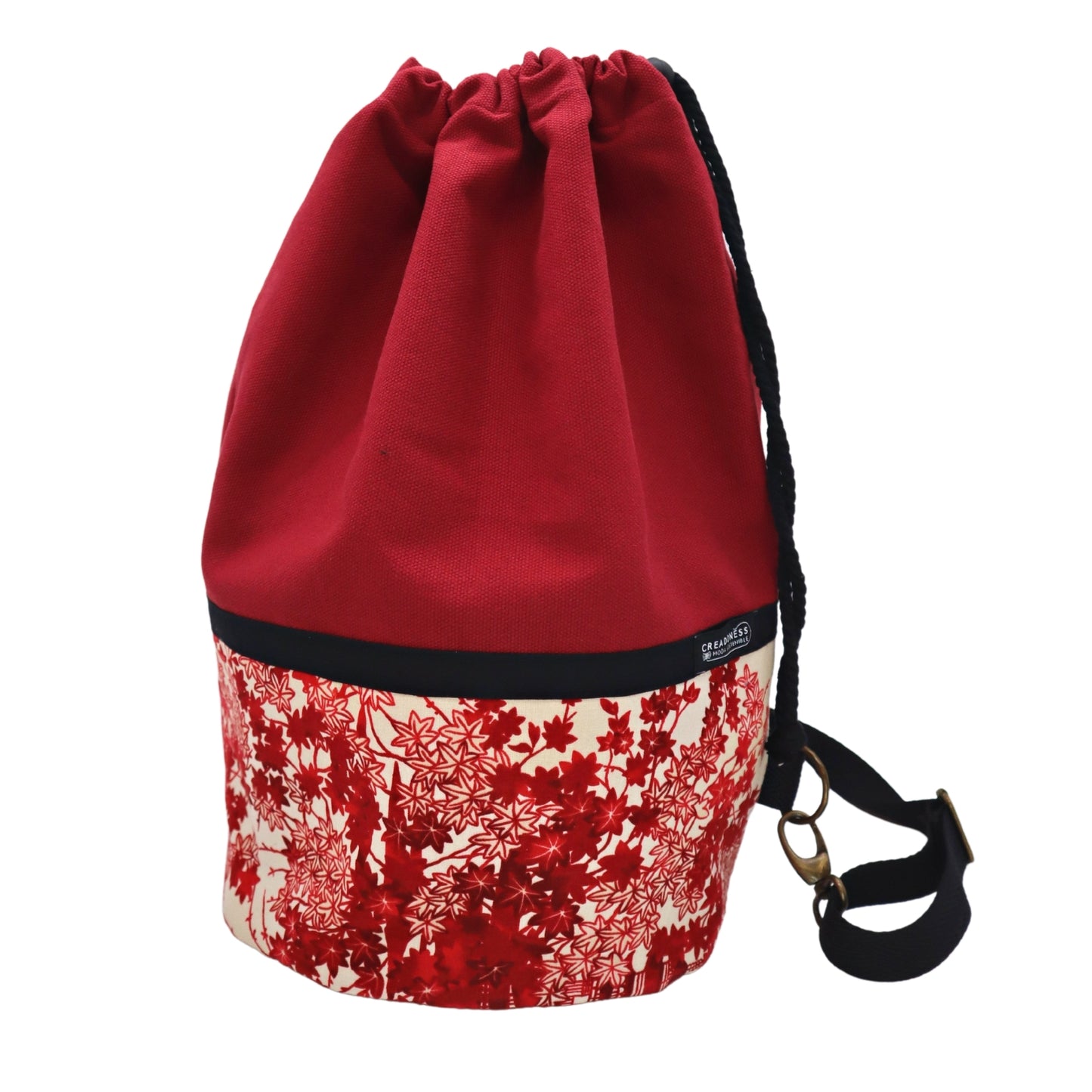 Mochila Petate de base circular de 24 cm de diámetro hecha de algodón. Su medida es de 38 cm de alto y 37 cm de ancho. Posee un asa bandolera para cruzar. En el interior tiene un bolsillo de 26 cm y un bolsillo oculto de 15 cm de profundidad.