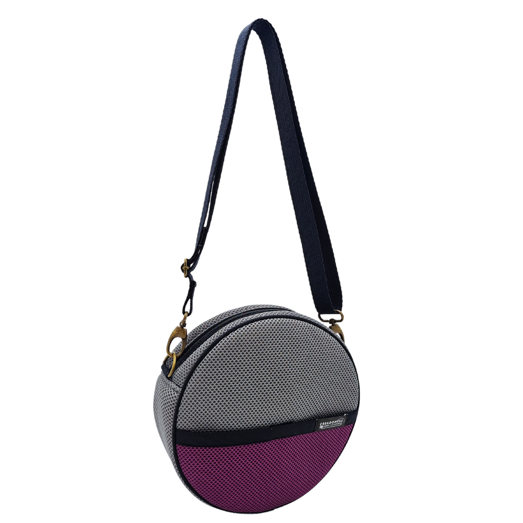 Compra nuestro bolso circular gris-violeta, hecho a mano con tejido 3D y material reciclado, elaborado artesanalmente por las mujeres del Programa Social de Creadoness.