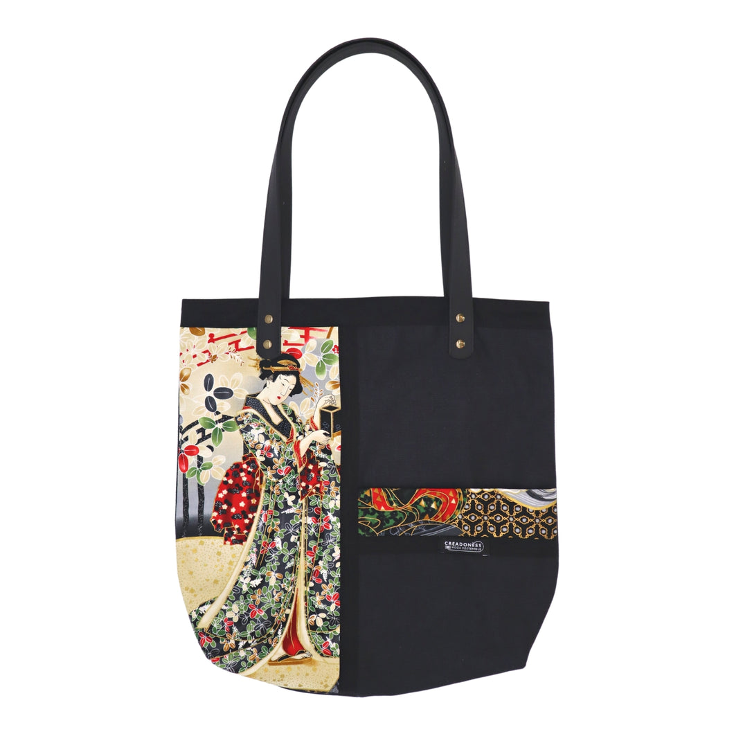 Tote Bag hecha de algodón de color negro. Tiene una estampa que cubre el lado derecho con un diseño japonés que muestra a una geisha bajo una lluvia de pétalos de flores. Posee dos asas de cuerina negra de 70 cm. 