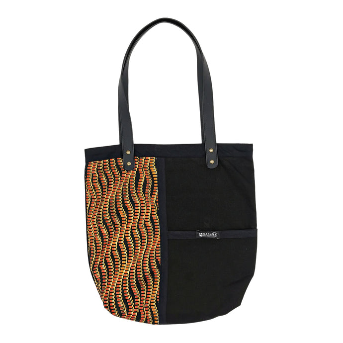 Tote Bag hecha de algodón de color negra. Tiene una estampa que cubre el lado derecho con un diseño de líneas horizontales onduladas de color naranja y amarillo. Posee dos asas de cuerina negra de 70 cm.